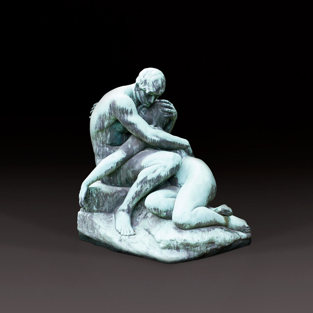 A sculpture depicts two human figures in a close embrace, rendered in muted green and blue tones. The sculpture depicts a visible, emotional moment between the two figures as they sit on a rocky surface. The artwork could have come from an art auction and displays fine details in the depiction of the human.