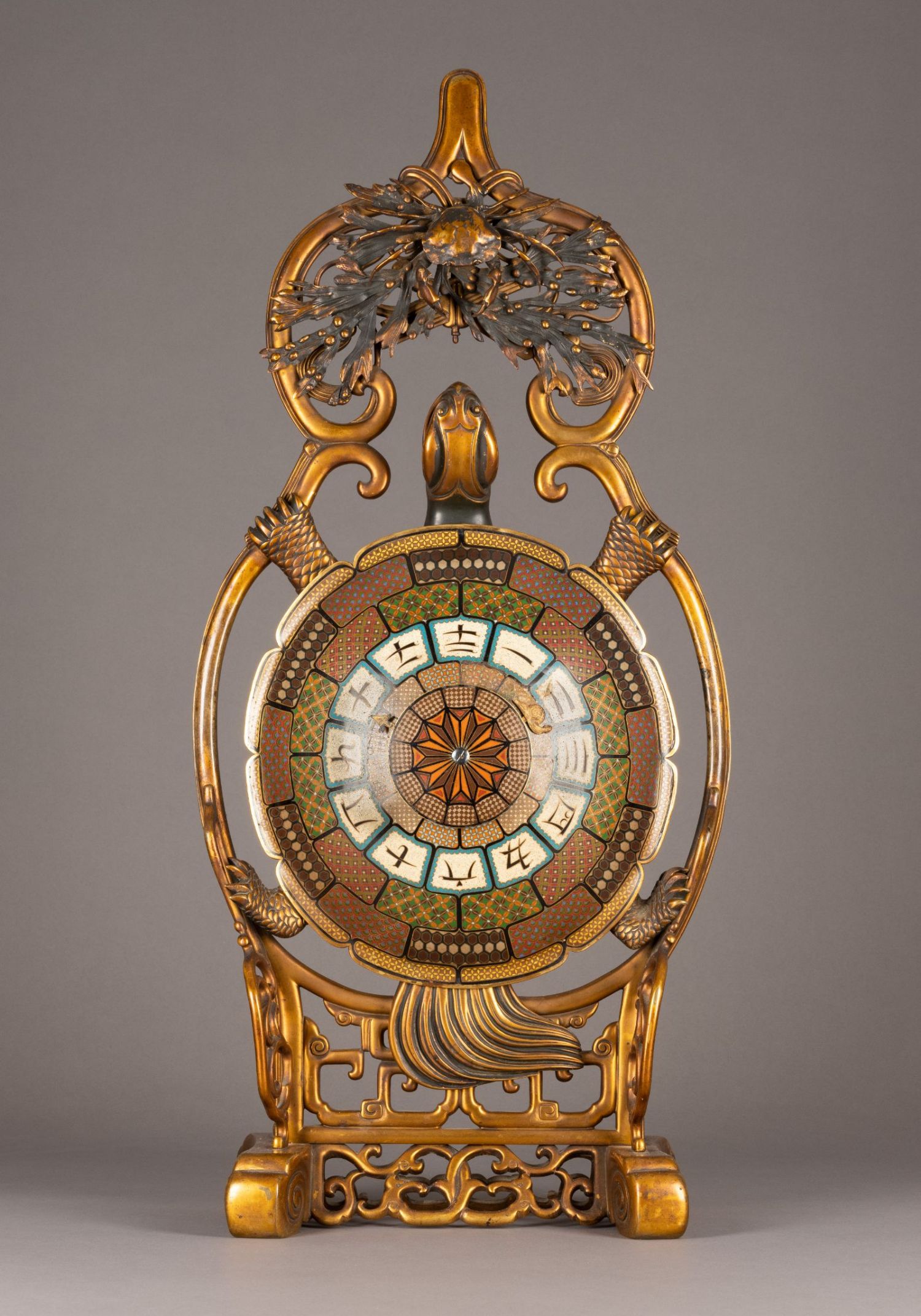 Kunstvoller antiker Rahmen mit eingebettetem Ziffernblatt, gestaltet in einem aufwendigen Jugendstil-Design aus goldfarbenem Metall mit feinen Verzierungen und Motiven natürlicher Elemente wie Blätter und Wellen. Im Zentrum befindet sich ein rundes, geometrisch gemustertes Ziffernblatt mit Zahlen und Symbolen.