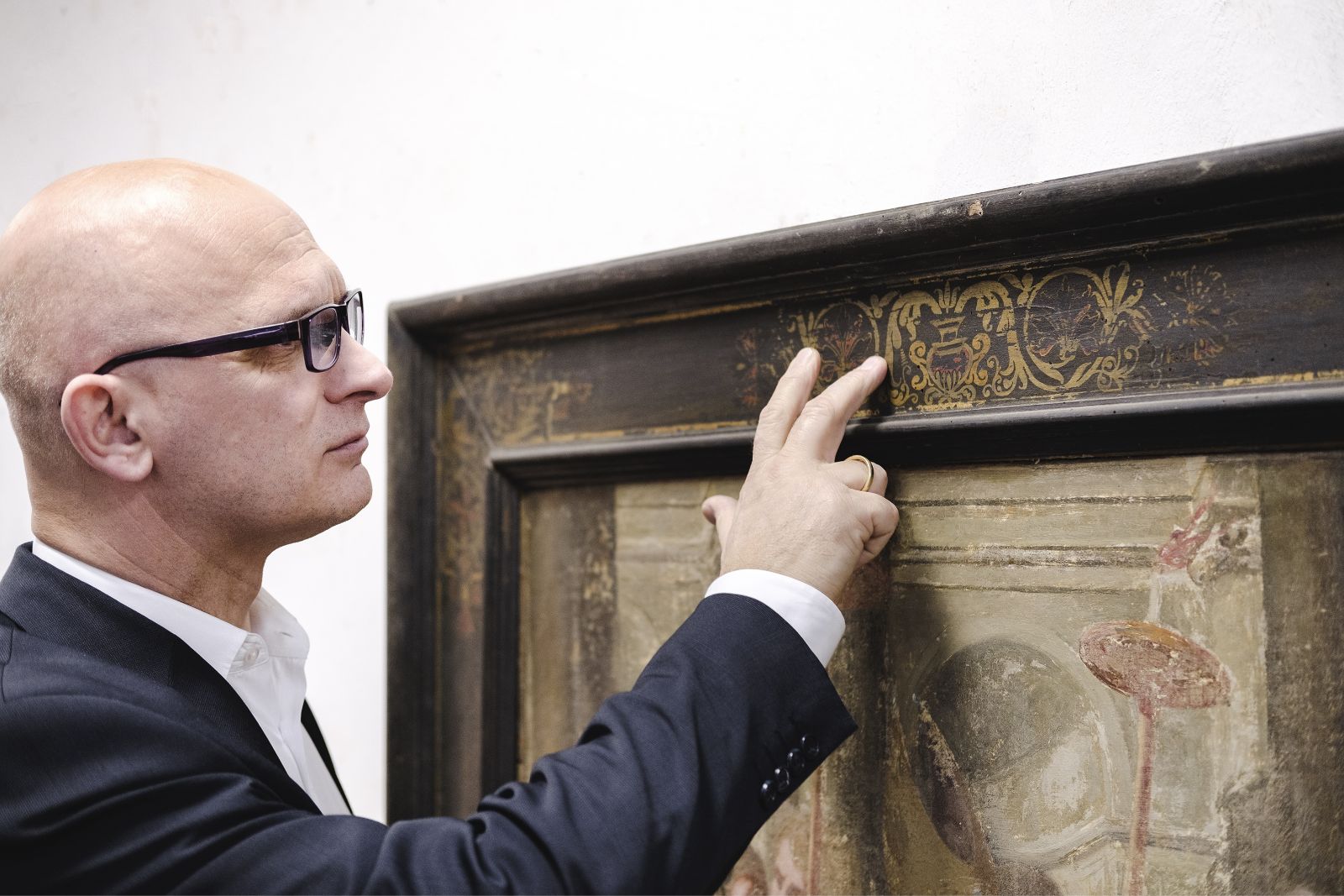 Mann in formeller Kleidung untersucht sorgfältig den Rahmen eines alten Gemäldes.
