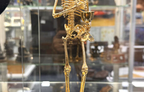 Goldene Skulptur eines Skeletts mit Kelch bei einer Kunstauktion, präsentiert in einer Vitrine.